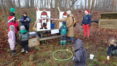 En gruppe børn og forældrene står rundt omkring en aktivitetszone, som har to julemænd malet på en flad styk træ - leget hedder flødebollekast